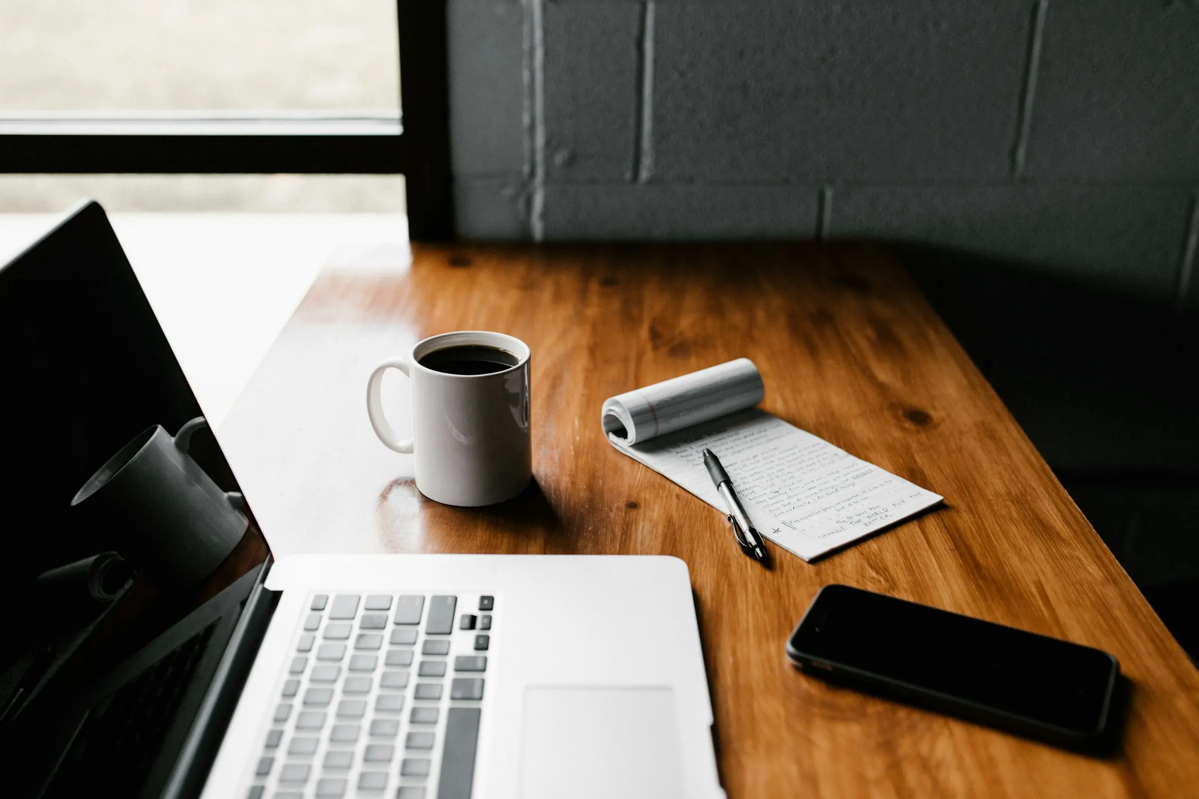 Laptop, coffee mug, notepad and phone on a wooden desk